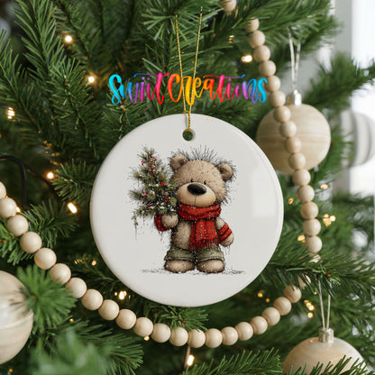 teddy bear in a red scarf holding a Christmas tree ceramic Christmas ornament hanging on a green Christmas tree
