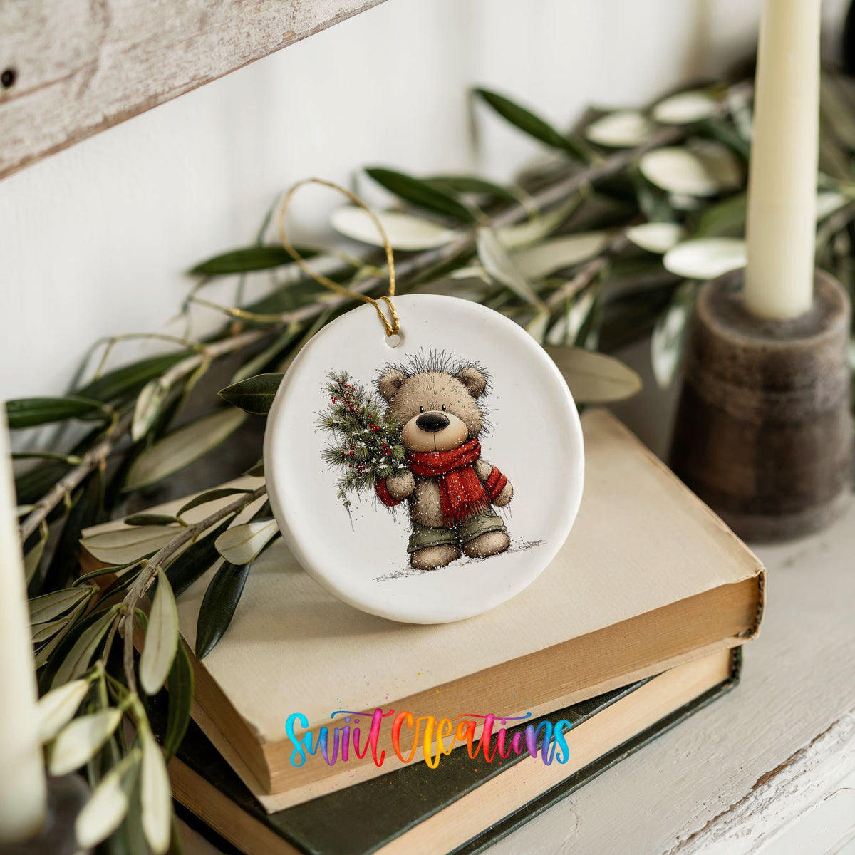 teddy bear in a red scarf holding a Christmas tree ceramic Christmas ornament styled on stacked books with greenery