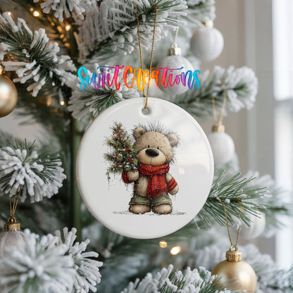 teddy bear in a red scarf holding a Christmas tree ceramic Christmas ornament hanging on a frosted Christmas tree