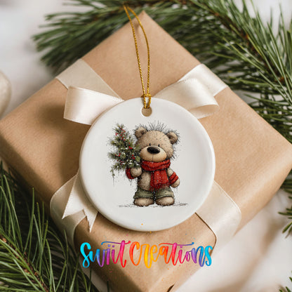 teddy bear in a red scarf holding a Christmas tree ceramic Christmas ornament displayed on a wrapped Christmas gift