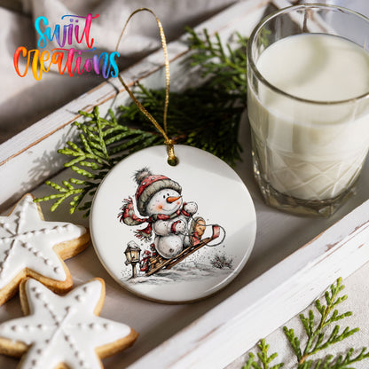snowman riding a wooden sled ceramic Christmas ornament styled with holiday cookies and a candle