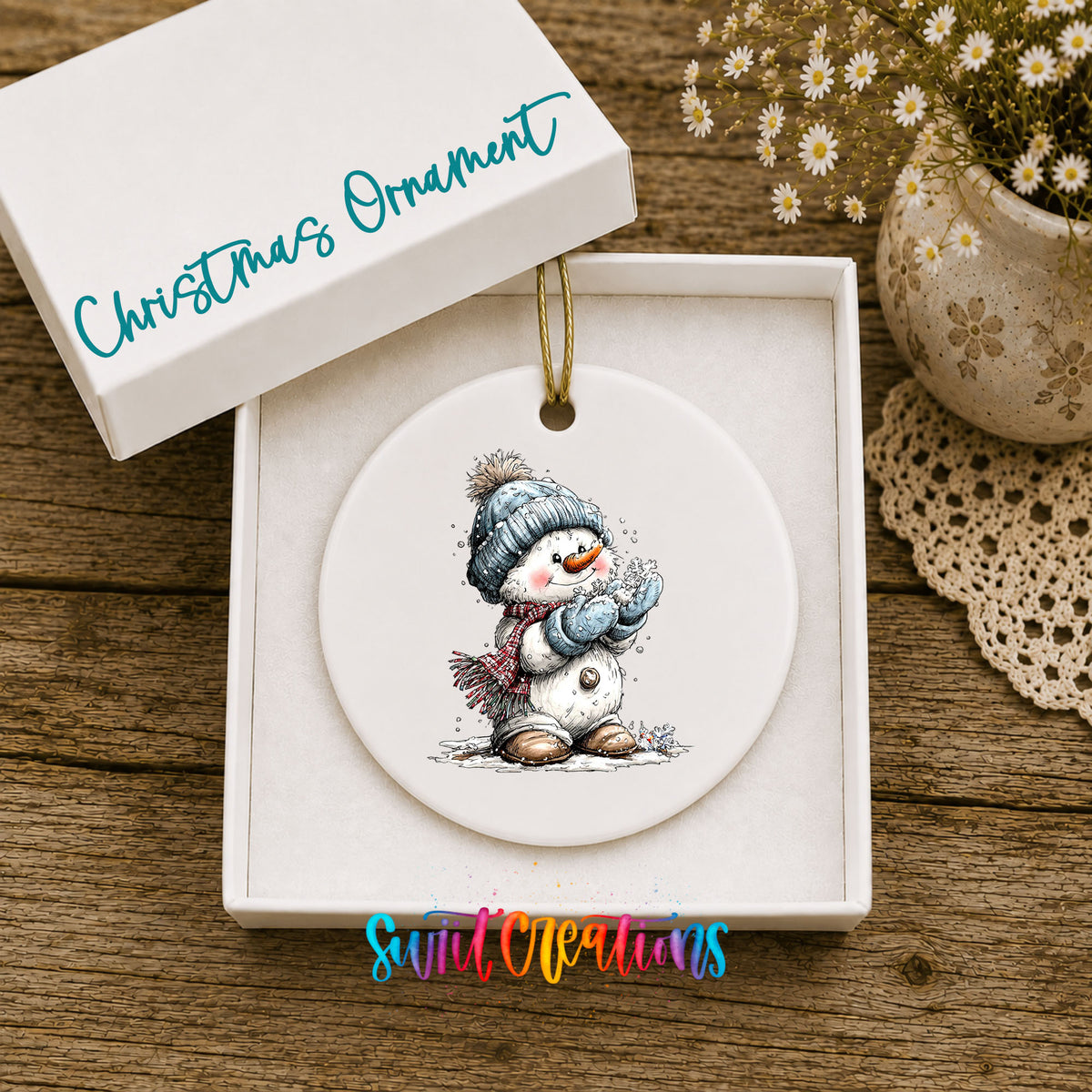 snowman in a blue hat holding a snowball ceramic Christmas ornament presented in a gift box