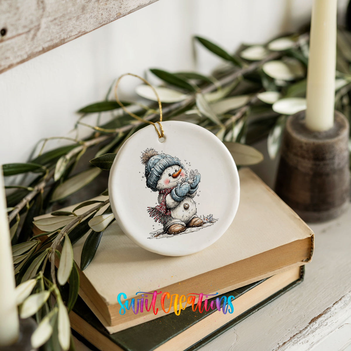 snowman in a blue hat holding a snowball ceramic Christmas ornament styled on stacked books with greenery