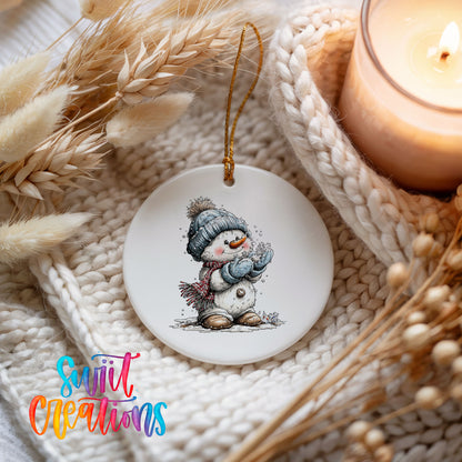 snowman in a blue hat holding a snowball ceramic Christmas ornament styled on a cozy knit blanket