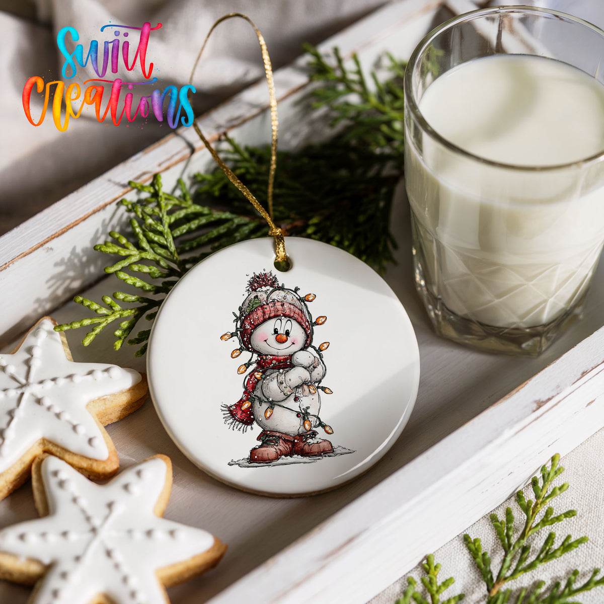 snowman in a red hat and striped scarf ceramic Christmas ornament styled with holiday cookies and a candle