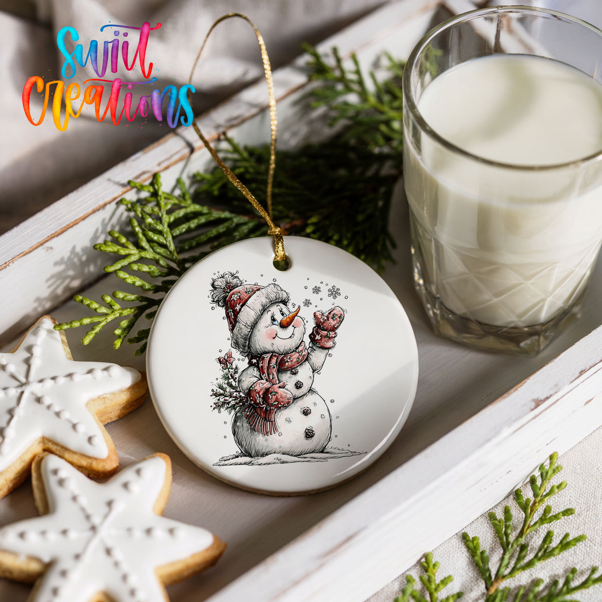 snowman holding a snowy Christmas tree ceramic Christmas ornament styled with holiday cookies and a candle