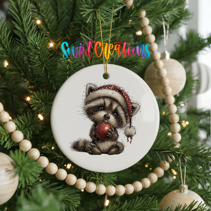 woodland raccoon in a Santa hat holding a red ornament ceramic Christmas ornament hanging on a green Christmas tree