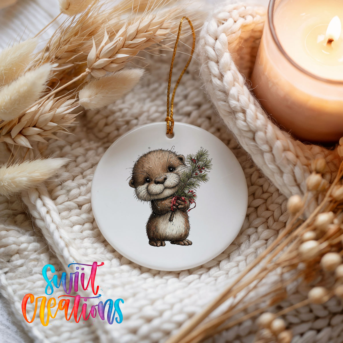 woodland otter holding a snowy pine branch ceramic Christmas ornament styled on a cozy knit blanket