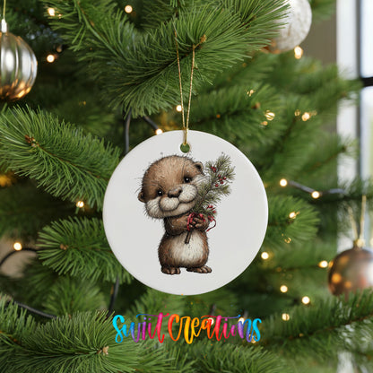 woodland otter holding a snowy pine branch ceramic Christmas ornament hanging on a lit Christmas tree