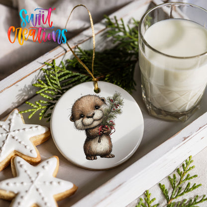 woodland otter holding a snowy pine branch ceramic Christmas ornament styled with holiday cookies and a candle