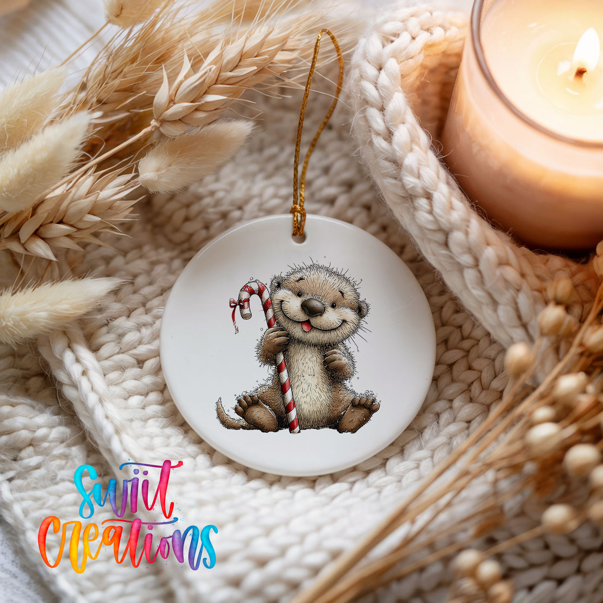 woodland otter holding a striped candy cane ceramic Christmas ornament styled on a cozy knit blanket