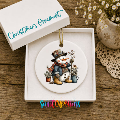 snowman in a black top hat beside potted evergreens ceramic Christmas ornament presented in a gift box