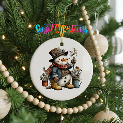snowman in a black top hat beside potted evergreens ceramic Christmas ornament hanging on a green Christmas tree