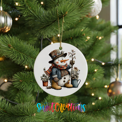 snowman in a black top hat beside potted evergreens ceramic Christmas ornament hanging on a lit Christmas tree