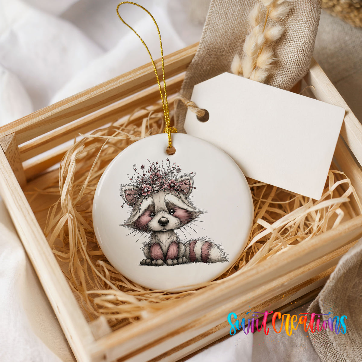 woodland raccoon wearing a pink winter bow ceramic Christmas ornament displayed in a wooden gift crate