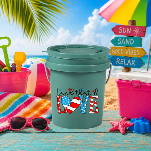 Land That I Love UV DTF transfer on a teal mini bucket on the beach