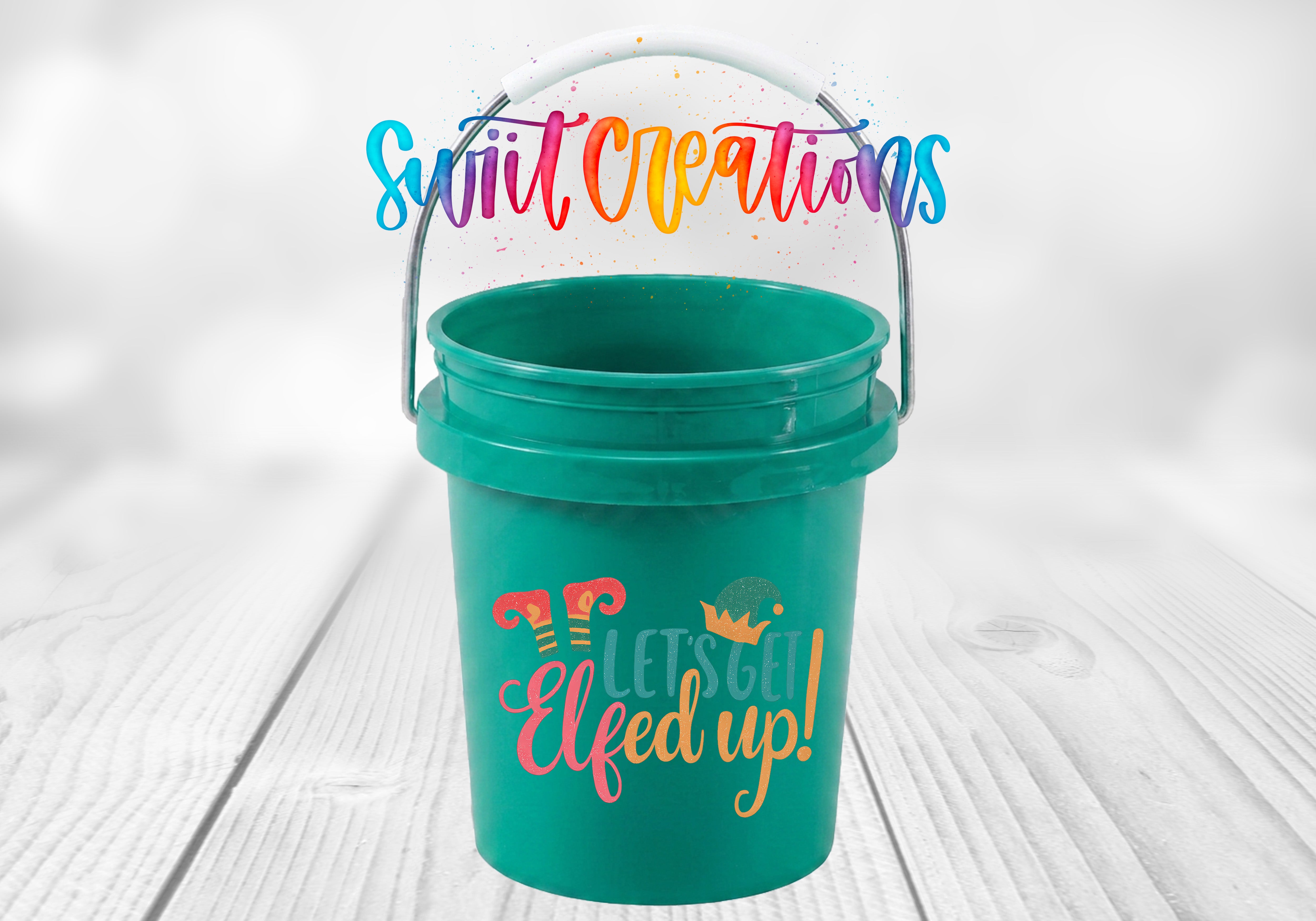 Let's Get Elfed Up Mini Bucket UV DTF Transfer with coral, teal, and golden orange lettering, striped elf legs, and an elf hat on a teal mini bucket displayed on a whitewashed wood surface