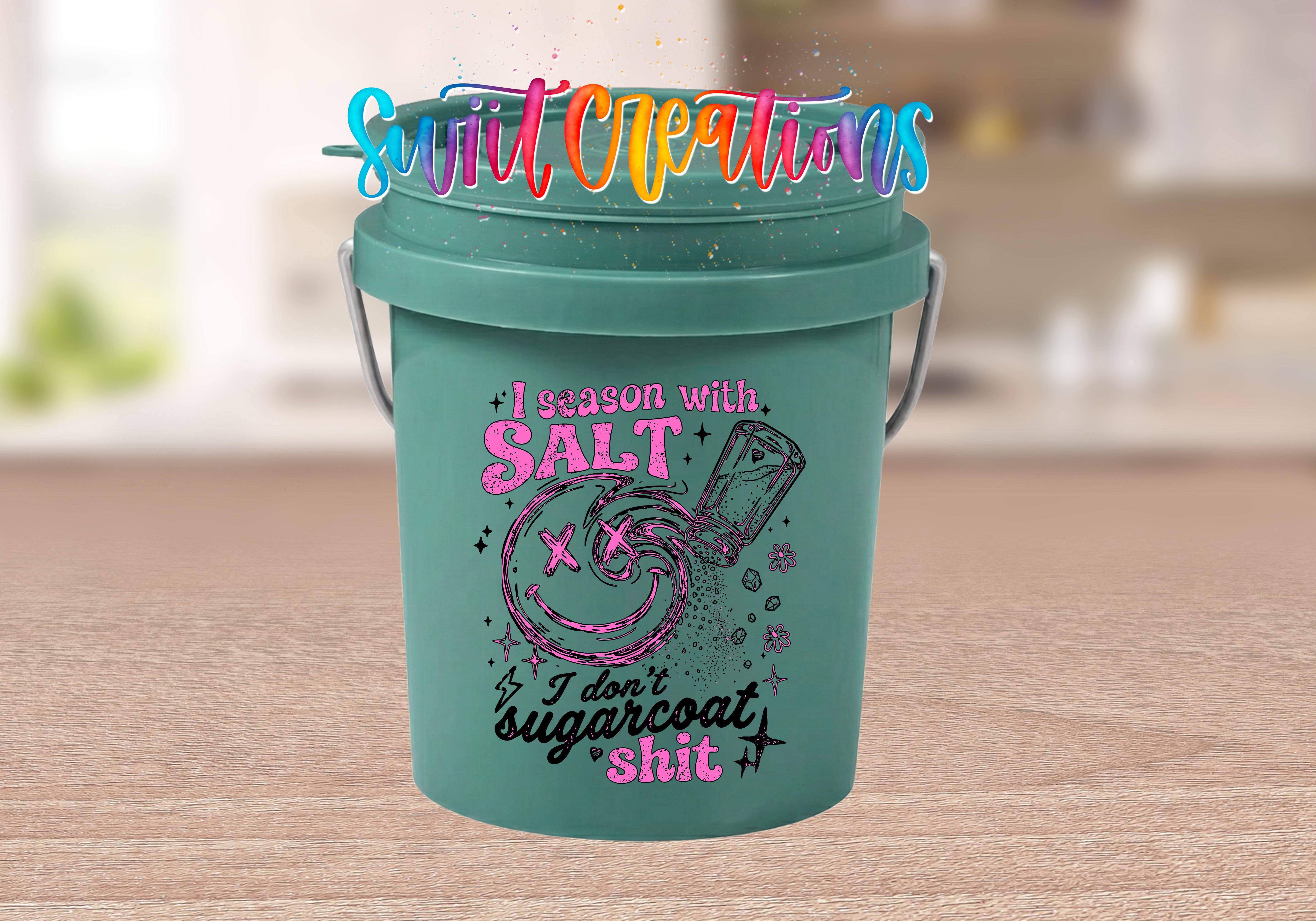 I Season with Salt Mini Bucket UV DTF Transfer with distressed pink and black quote, smiling face, salt shaker, stars, and flowers on a teal mini bucket displayed on a wood tabletop