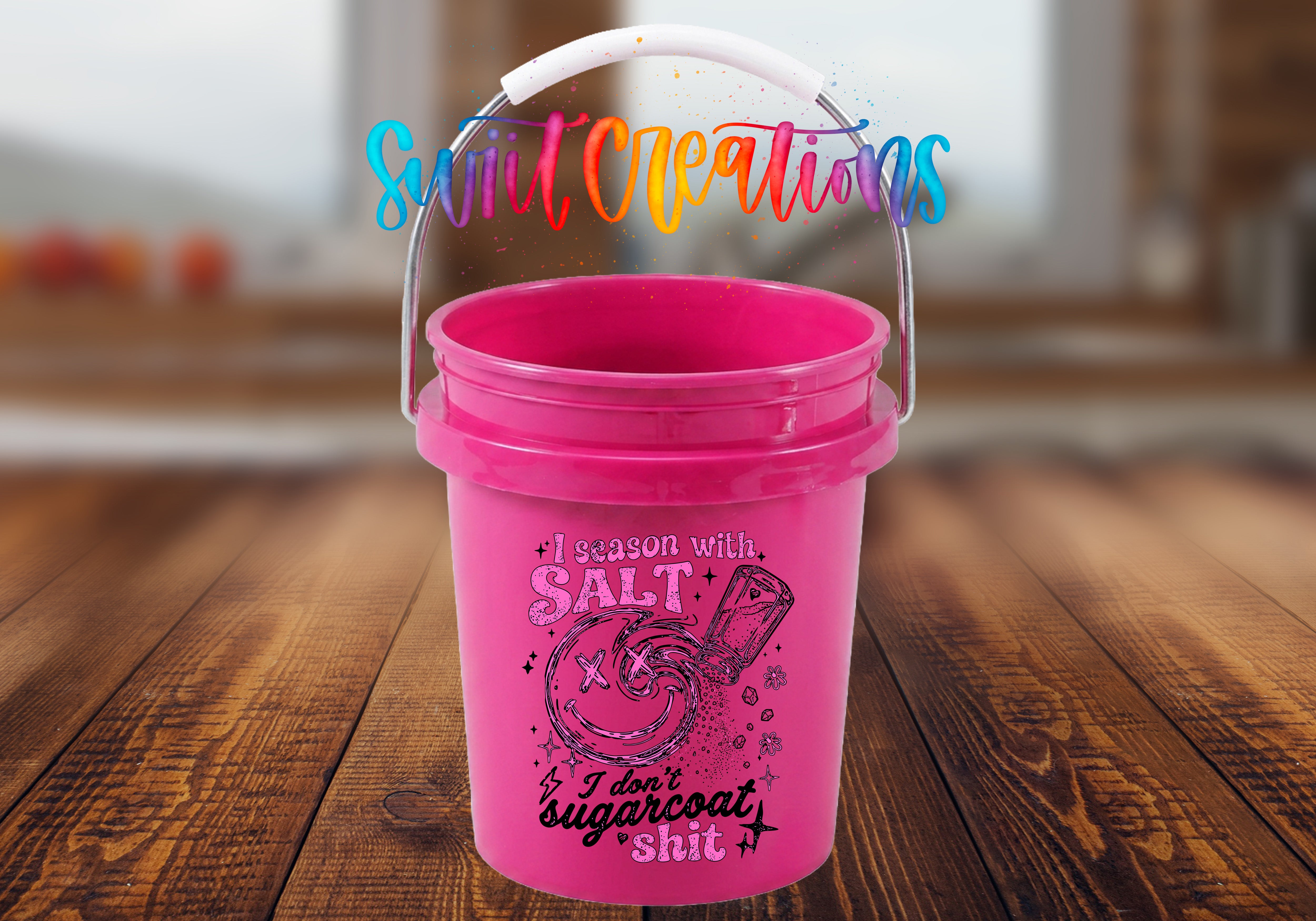 I Season with Salt Mini Bucket UV DTF Transfer with distressed pink and black quote, smiling face, salt shaker, stars, and flowers on a pink mini bucket with handle raised on a rustic wood tabletop