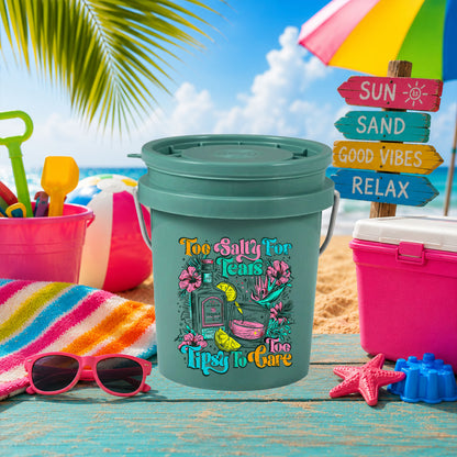 Too Salty for Tears Too Tipsy to Care UV DTF transfer on a teal mini bucket on the beach