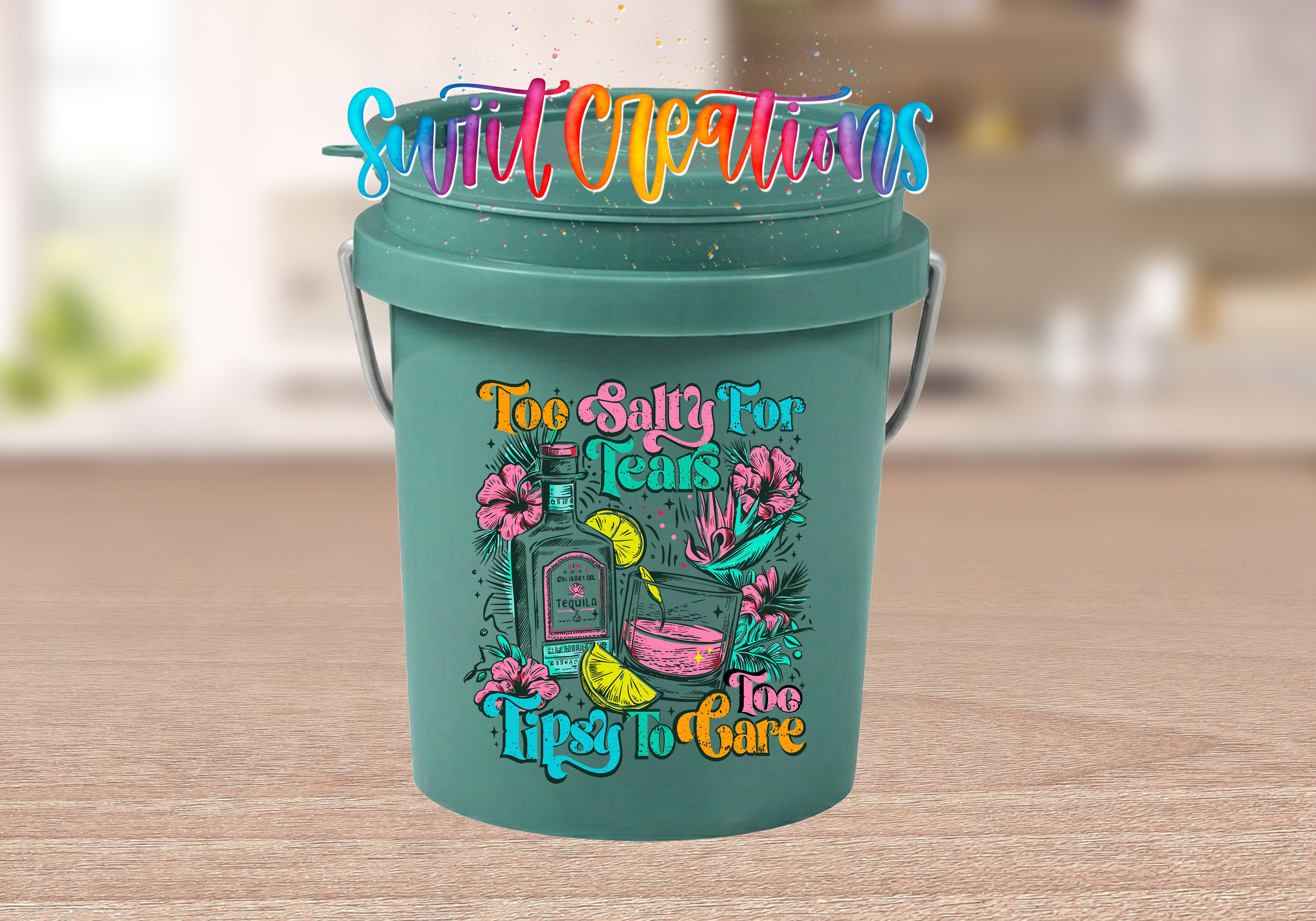 Too Salty for Tears Too Tipsy to Care Mini Bucket UV DTF Transfer with tequila bottle, cocktail, lime, tropical flowers, and colorful lettering on a teal mini bucket displayed on a wood tabletop