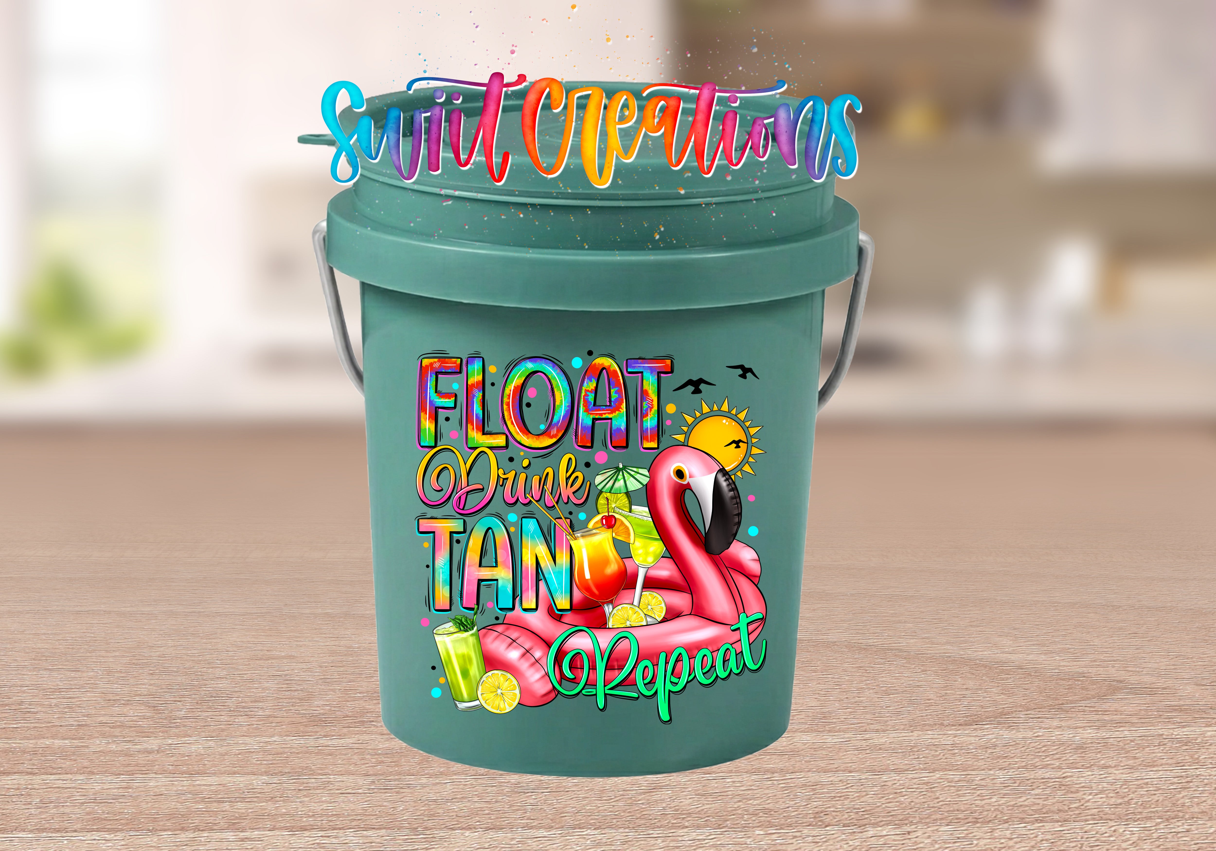 Float Drink Tan Repeat Mini Bucket UV DTF Transfer with rainbow lettering, pink flamingo pool float, tropical cocktails, citrus, sun, and birds on a teal mini bucket displayed on a wood tabletop