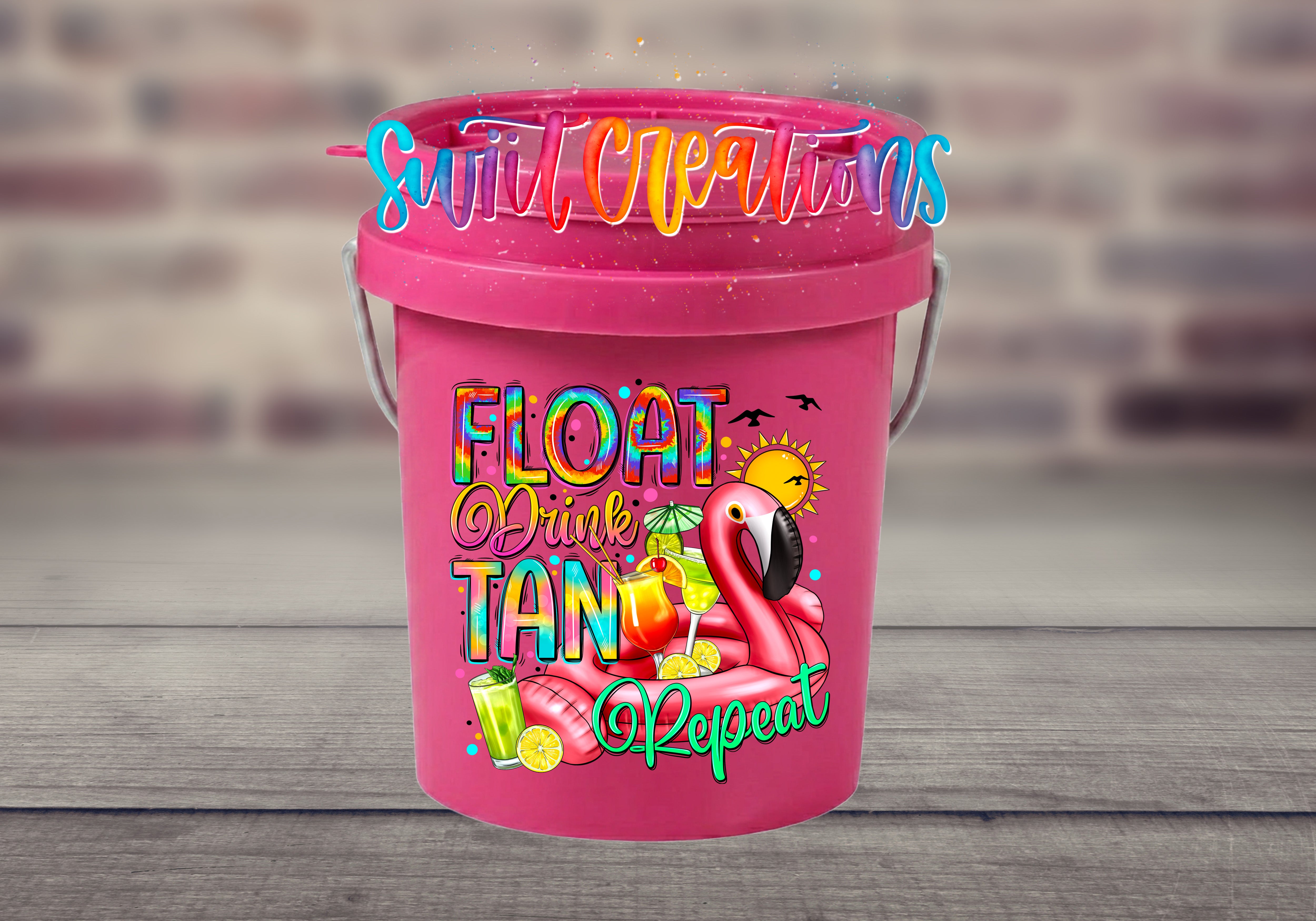 Float Drink Tan Repeat Mini Bucket UV DTF Transfer with rainbow lettering, pink flamingo pool float, tropical cocktails, citrus, sun, and birds on a pink mini bucket displayed on a gray wood surface