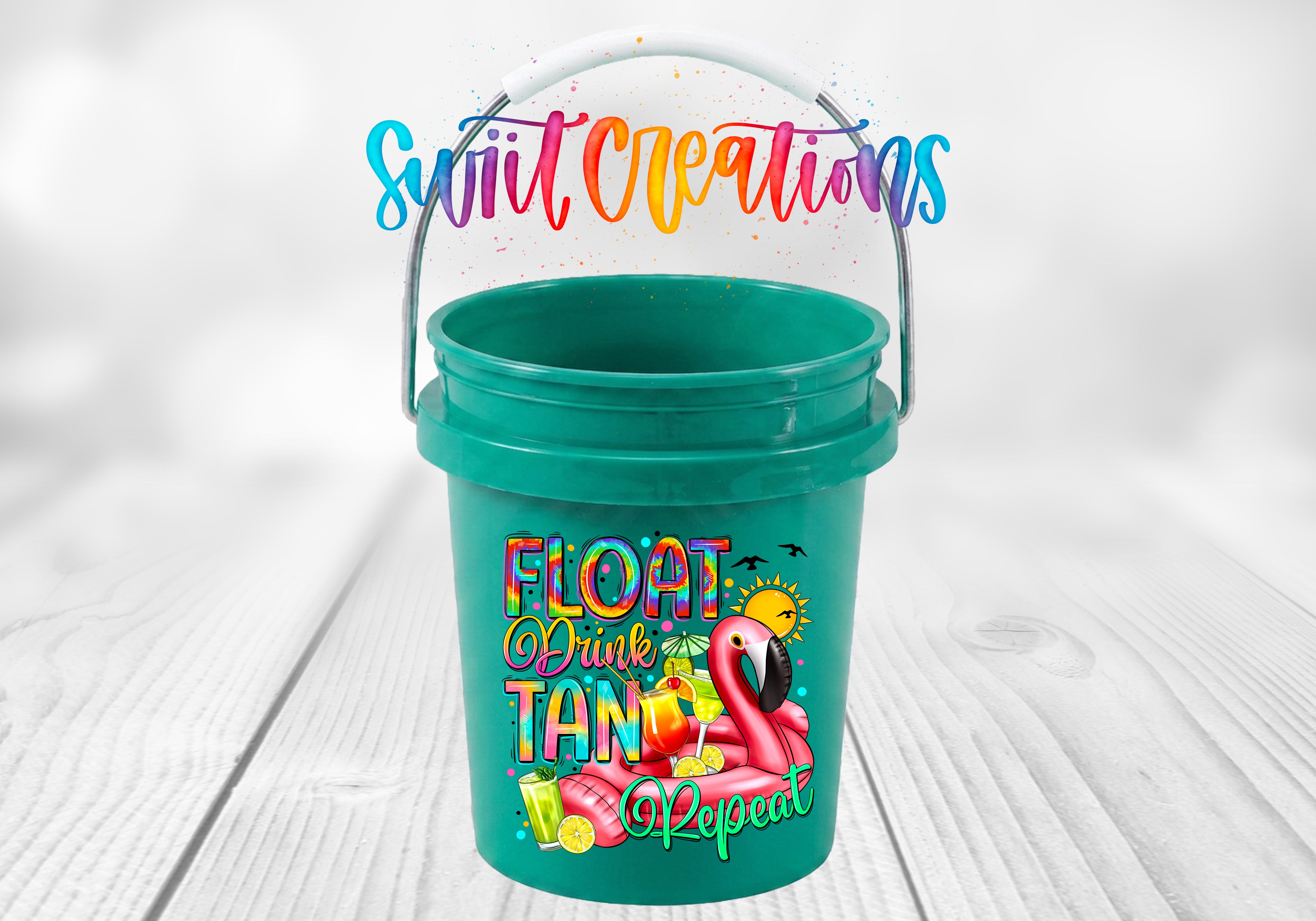 Float Drink Tan Repeat Mini Bucket UV DTF Transfer with rainbow lettering, pink flamingo pool float, tropical cocktails, citrus, sun, and birds on a teal mini bucket displayed on a whitewashed wood surface