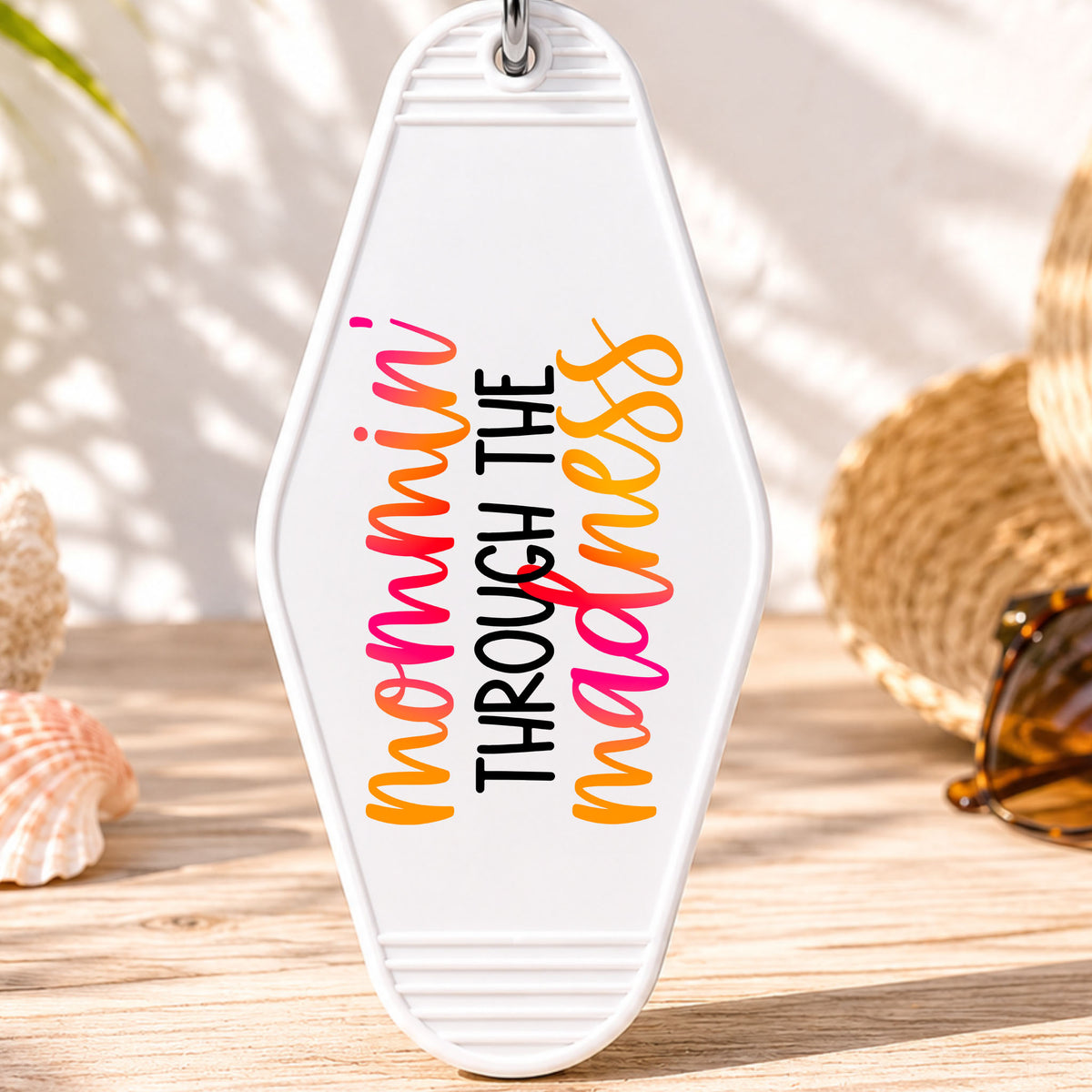 Mommin' Through the Madness UV DTF transfer on a white motel keychain with beach decor