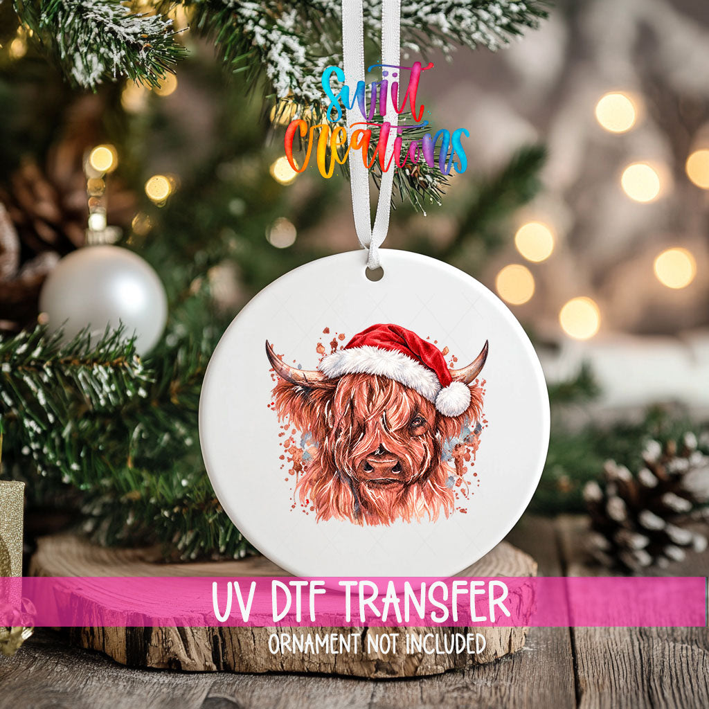 Highland Cow Santa Hat ornament UV DTF transfer on an ornament resting on a wood slice beside a Christmas tree