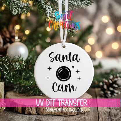 Santa Cam ornament UV DTF transfer on an ornament resting on a wood slice beside a Christmas tree