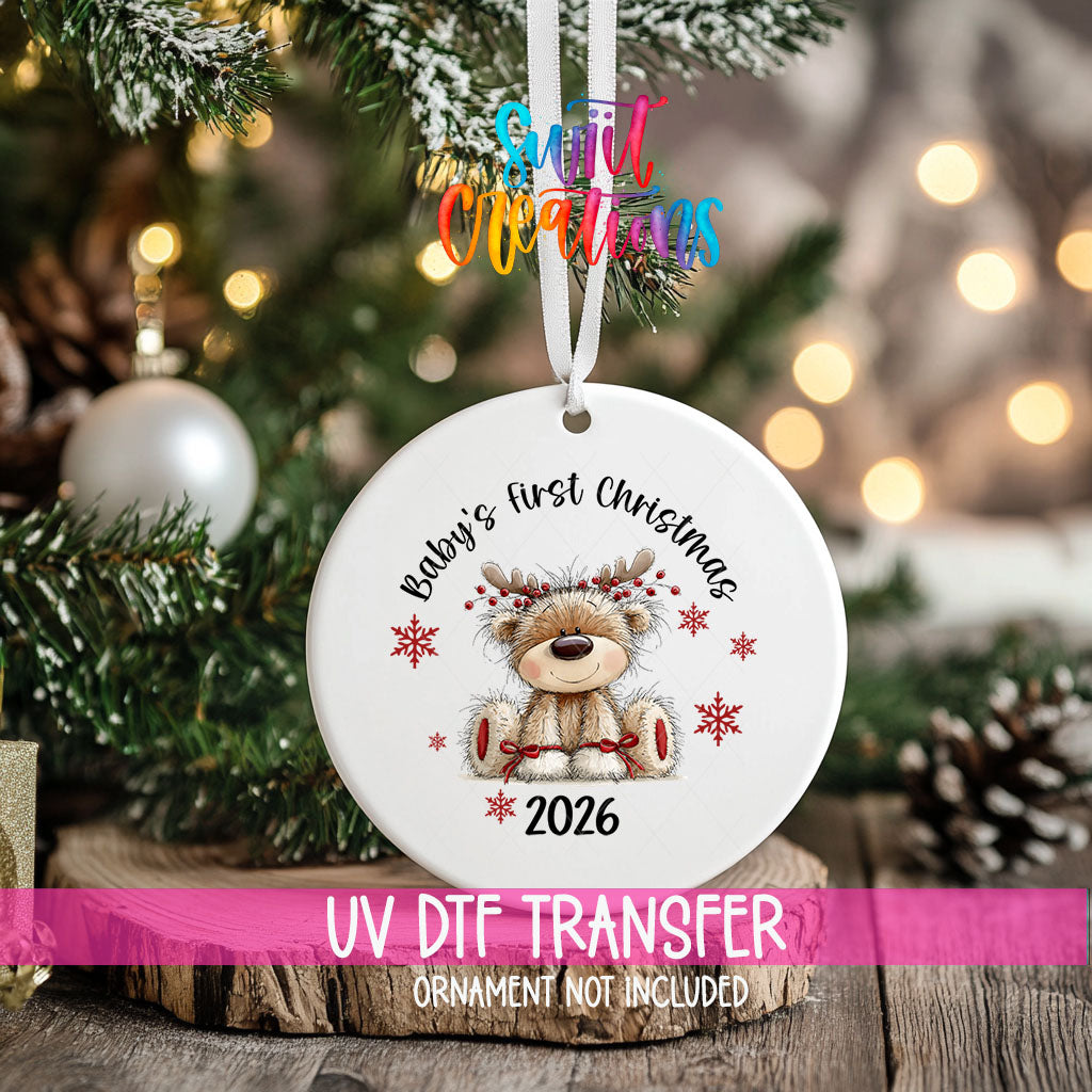 Baby's First Christmas ornament UV DTF transfer on an ornament resting on a wood slice beside a Christmas tree