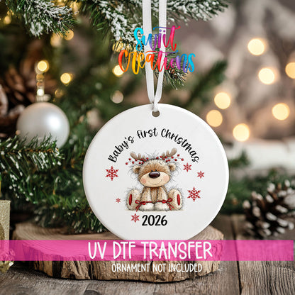 Baby's First Christmas ornament UV DTF transfer on an ornament resting on a wood slice beside a Christmas tree