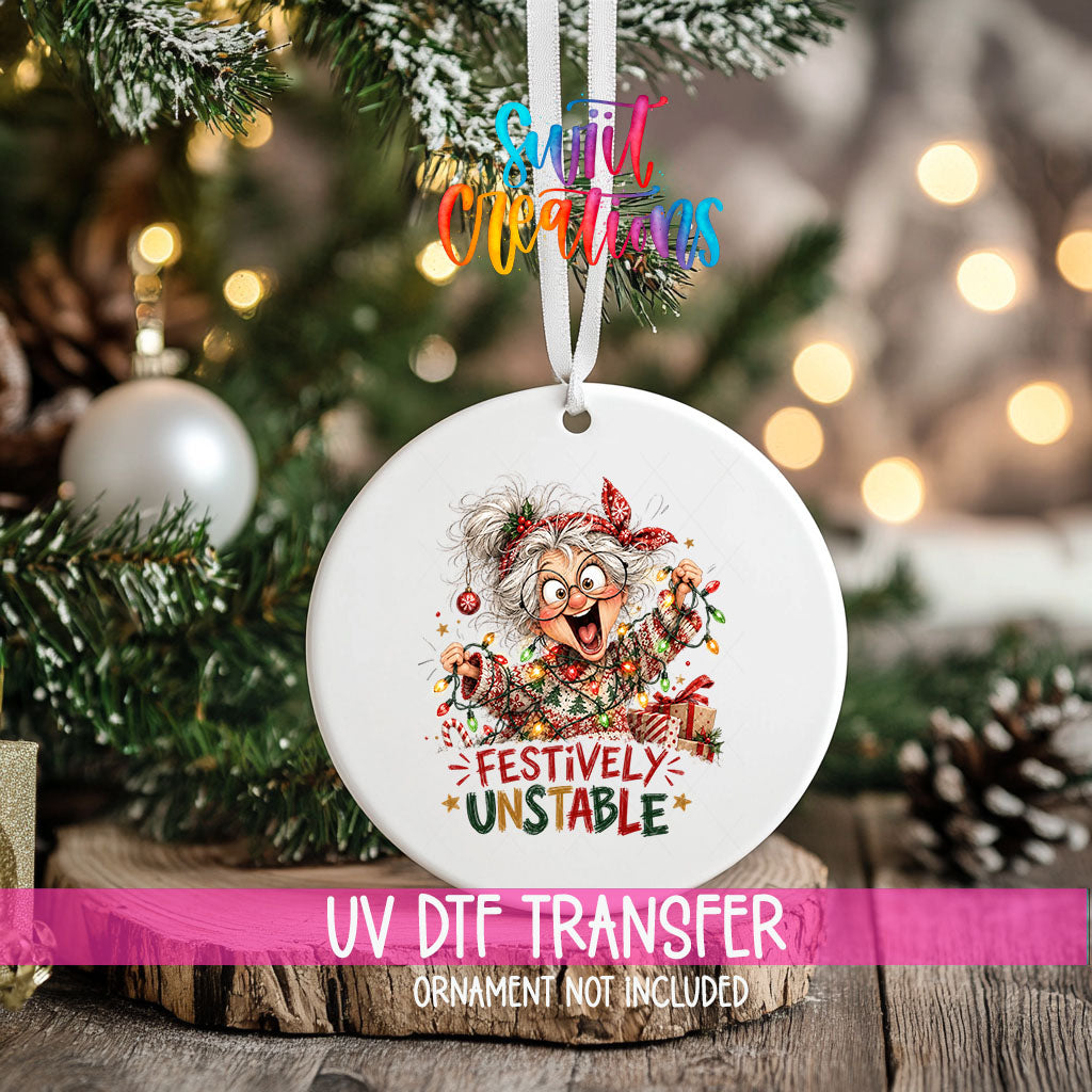Festively Unstable ornament UV DTF transfer on an ornament resting on a wood slice beside a Christmas tree