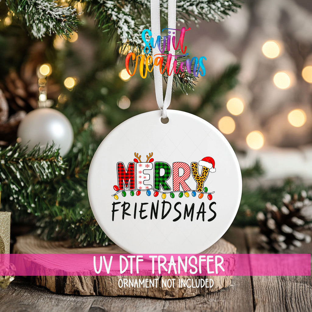 Merry Friendsmas ornament UV DTF transfer on an ornament resting on a wood slice beside a Christmas tree