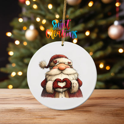 Cute Santa making heart hands ornament UV DTF transfer on an ornament on a wooden table with tree lights behind it
