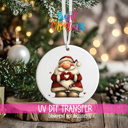 Cute standing Santa making heart hands ornament UV DTF transfer on an ornament resting on a wood slice beside a Christmas tree