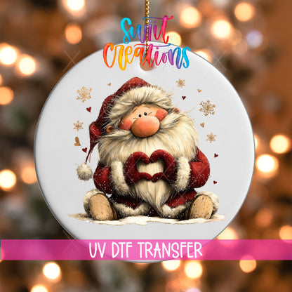 Cute sitting Santa making heart hands UV DTF transfer on a white ornament with a pink UV DTF Transfer banner and bokeh lights