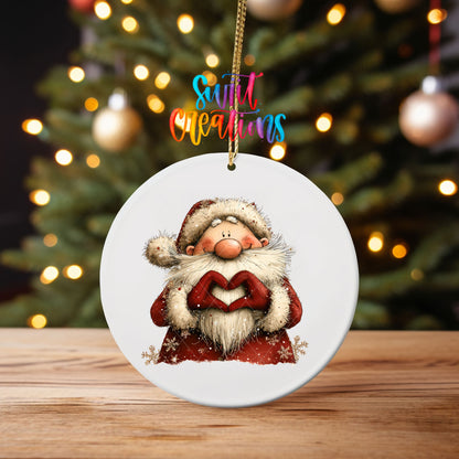 Cute Santa in a snowflake coat making heart hands ornament UV DTF transfer on an ornament on a wooden table with tree lights behind it