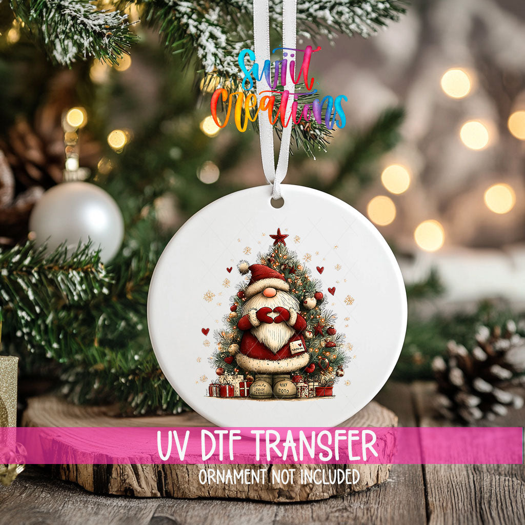 Cute Santa with a letter in front of a Christmas tree ornament UV DTF transfer on an ornament resting on a wood slice beside a Christmas tree