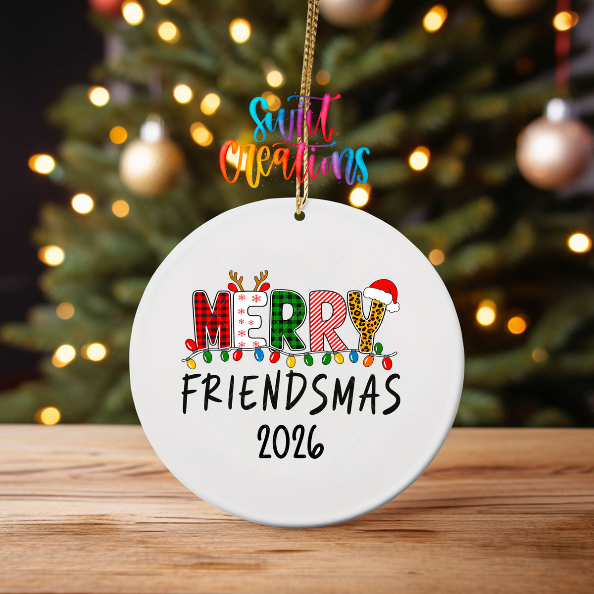 Merry Friendsmas 2026 ornament UV DTF transfer on an ornament on a wooden table with tree lights behind it
