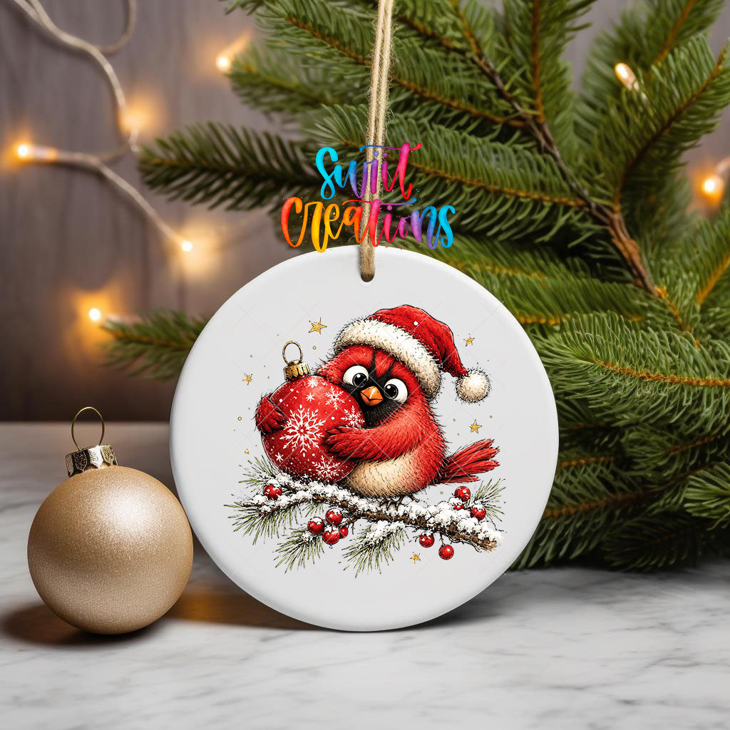 Santa hat cardinal hugging an ornament UV DTF transfer on an ornament beside a gold bauble and pine