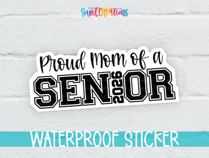 Proud Mom of a 2026 Senior sticker in black script and varsity letters on a white brick background with a waterproof sticker banner