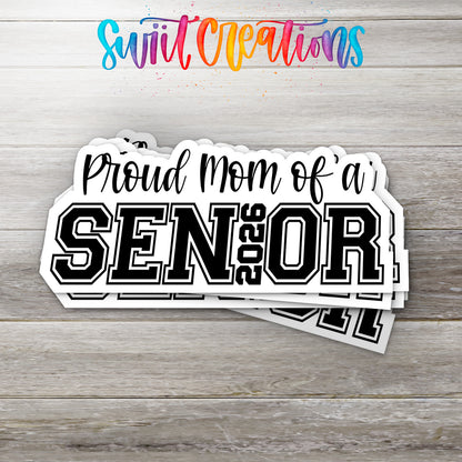 Stack of Proud Mom of a 2026 Senior glossy stickers on a gray wood table