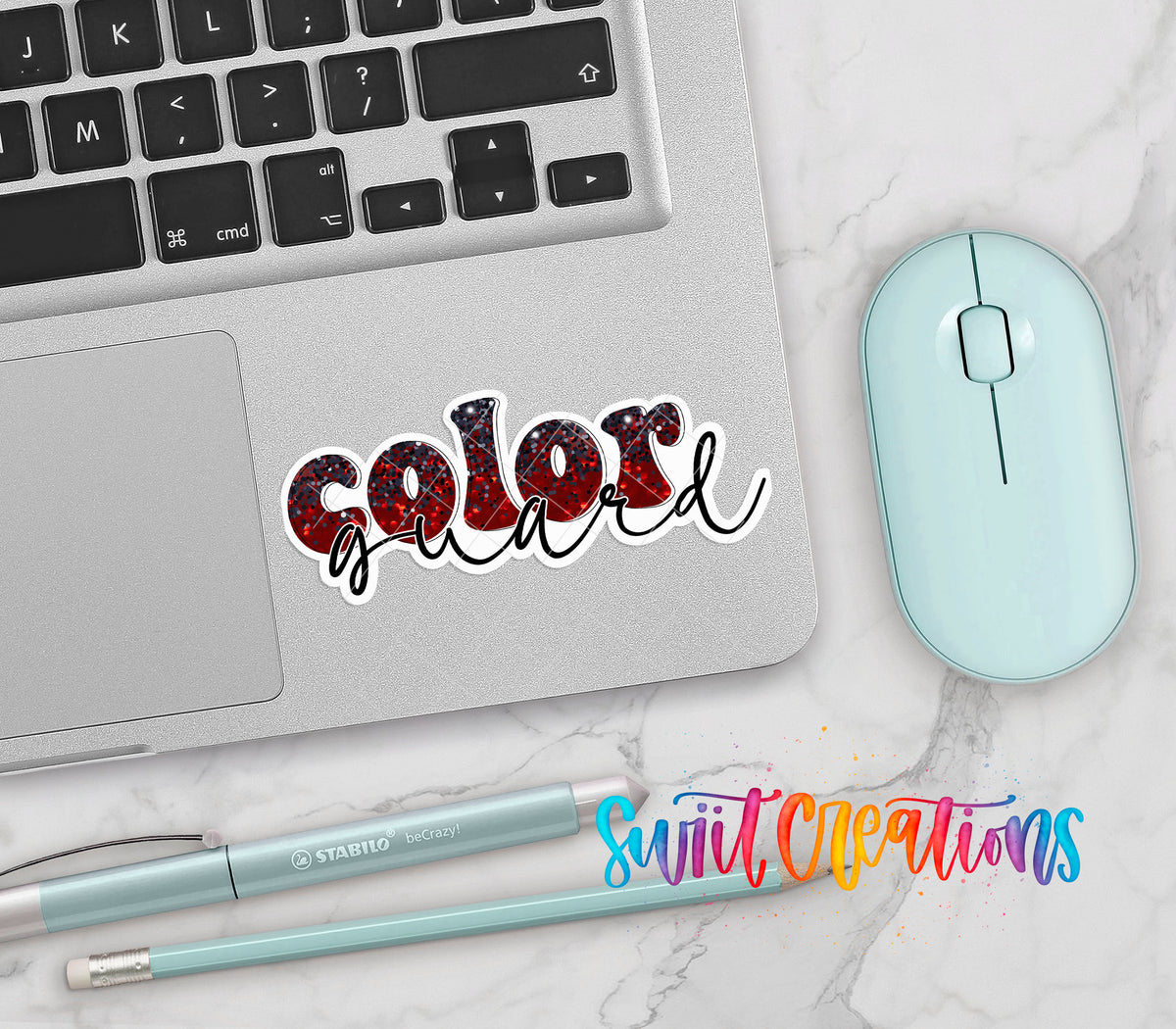 Red and black Color Guard vinyl sticker on a silver laptop next to a mint mouse and pens