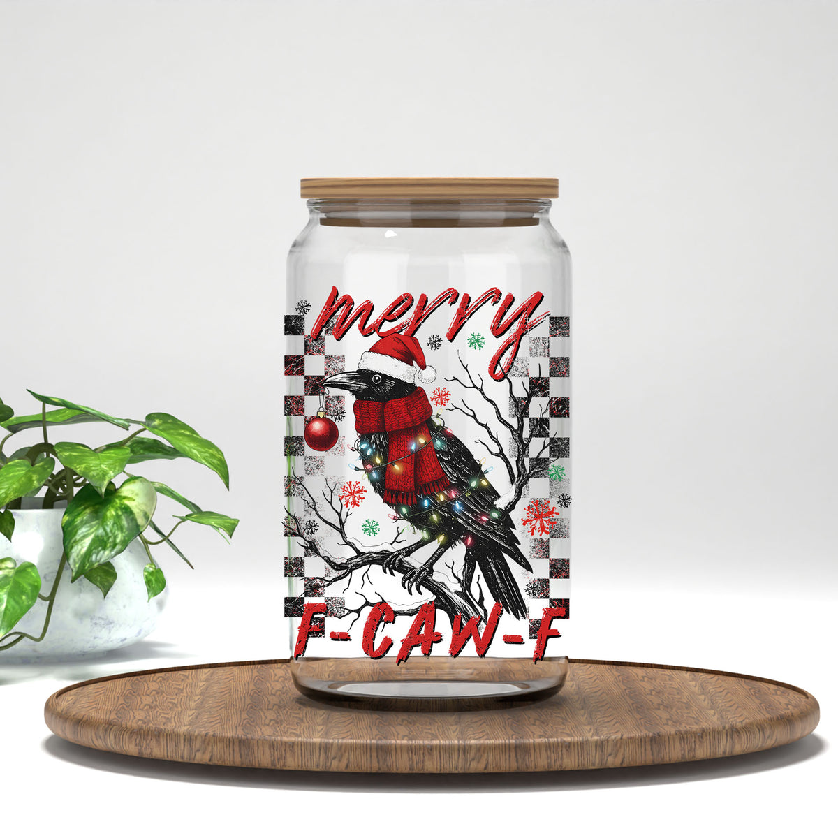 Merry F-CAW-F crow UV DTF transfer on a clear glass can on a wood tray with greenery