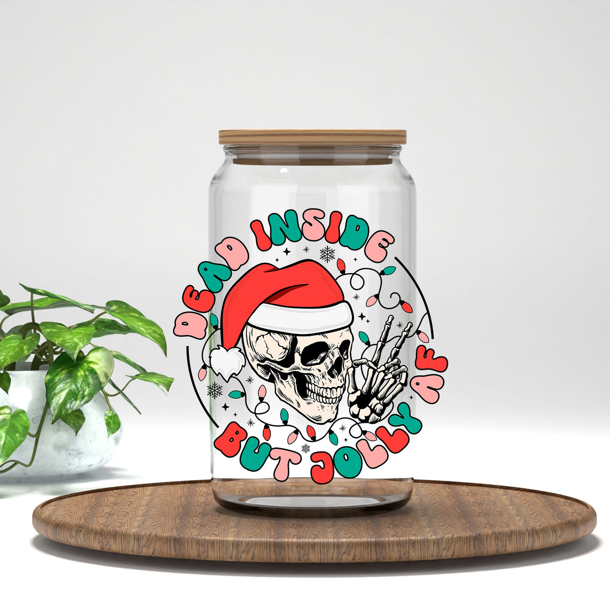 Dead Inside But Jolly AF skeleton UV DTF transfer on a clear glass can on a wood tray with greenery