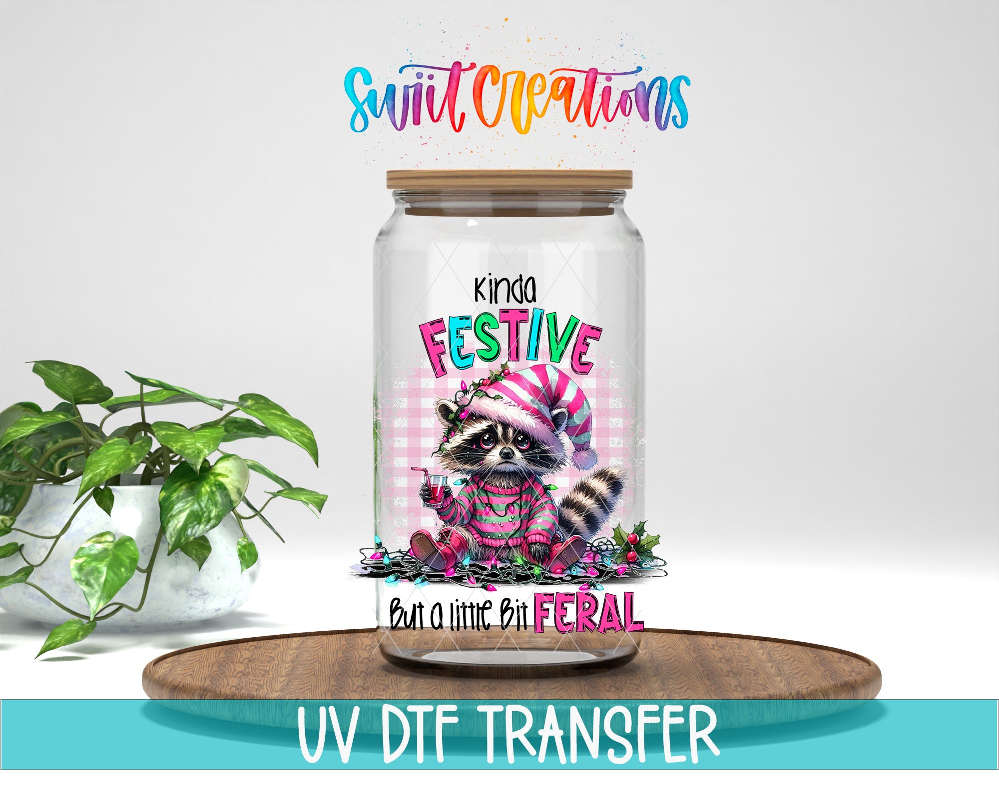 a glass jar with a raccoon wearing a festive hat and scarf, sitting on a wooden tray. The jar has a lid and is placed on a wooden surface. There is a potted plant in the background, and the image includes text that says "Swift Creations" and "UV DFT Transfer".
