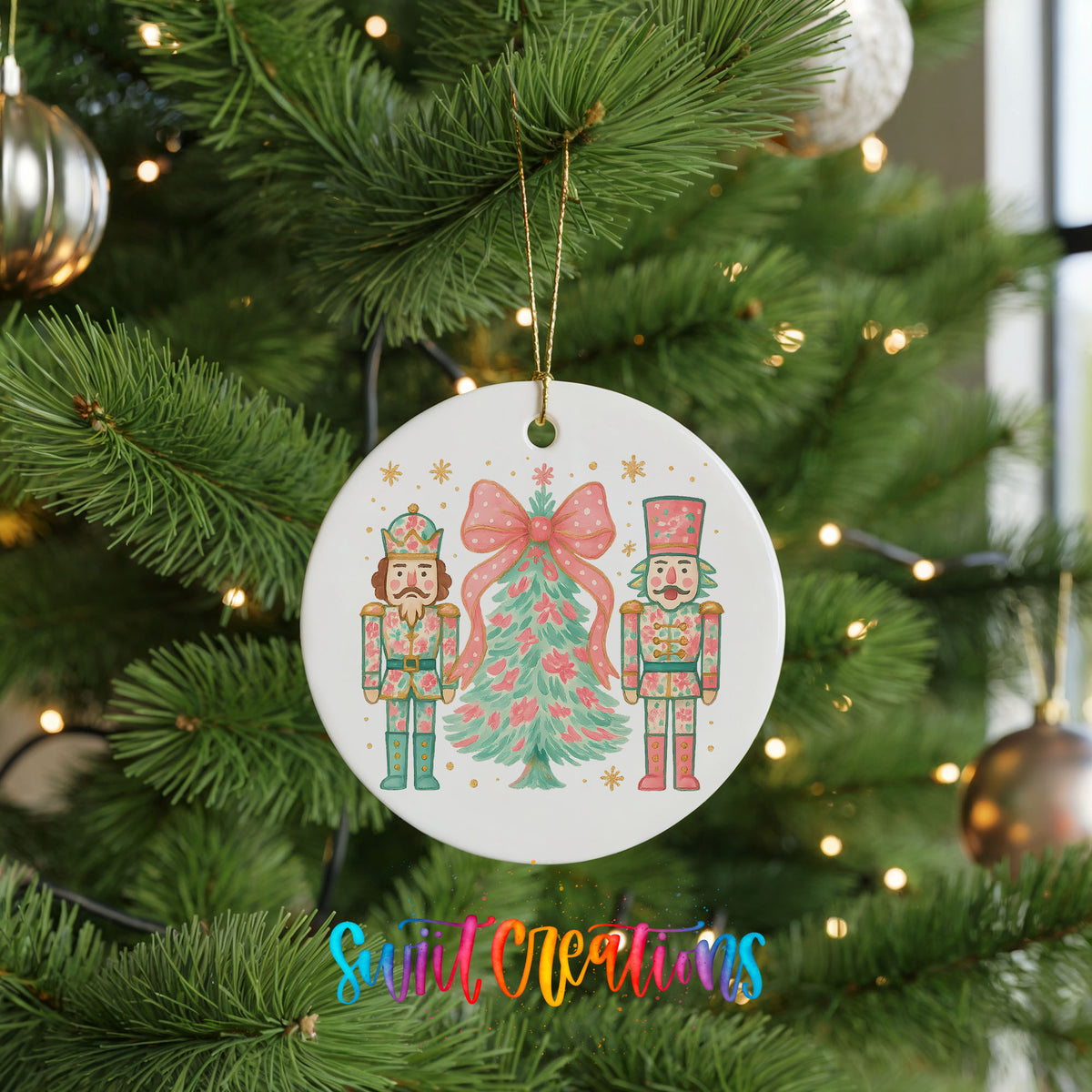 A white ornament with a Christmas tree and nutcracker figures is hanging on a pine tree, surrounded by ornaments and twinkling lights.
