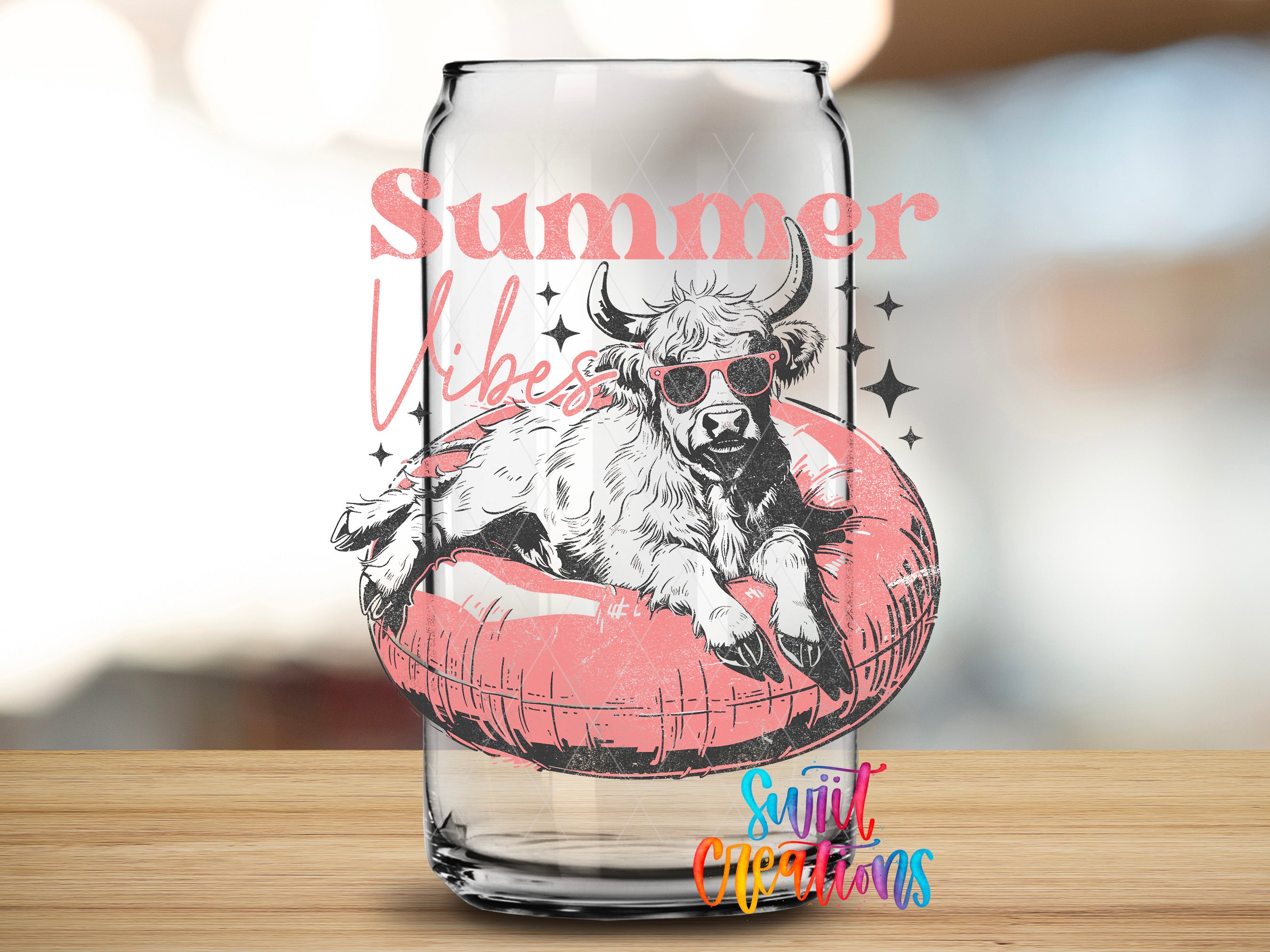 A glass can with a printed design featuring a cow wearing sunglasses and sitting on a red inner tube, with the text "Summer Vibes" and "Sunlit Creations" printed on it.